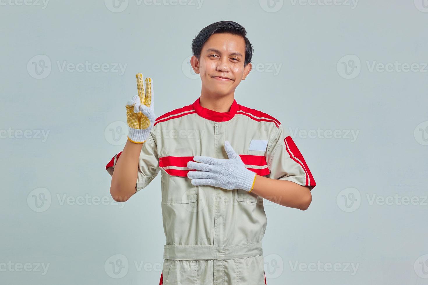 Portrait of handsome man wearing mechanical uniform swearing with hands on chest and making peace sign with fingers photo