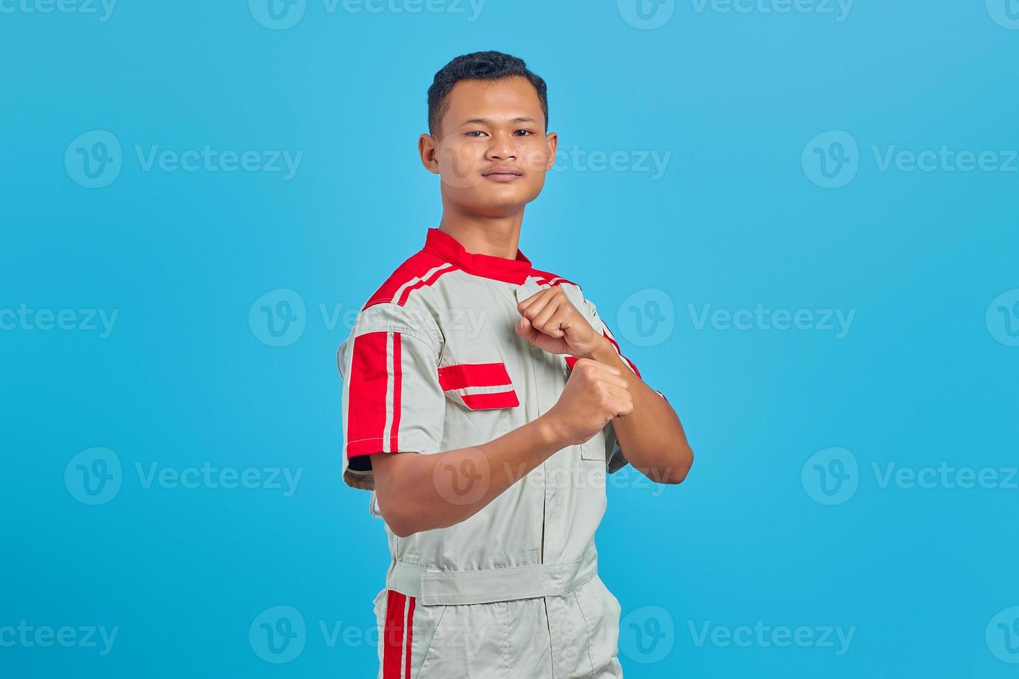 Portrait of angry young Asian mechanic showing boxer gesture over blue background photo