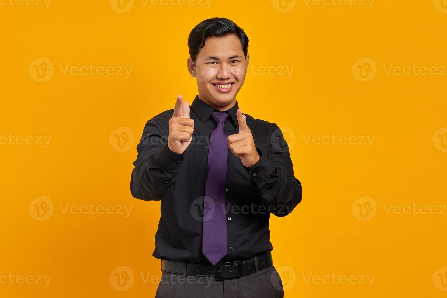 Handsome young businessman smiling while pointing at camera on yellow background photo