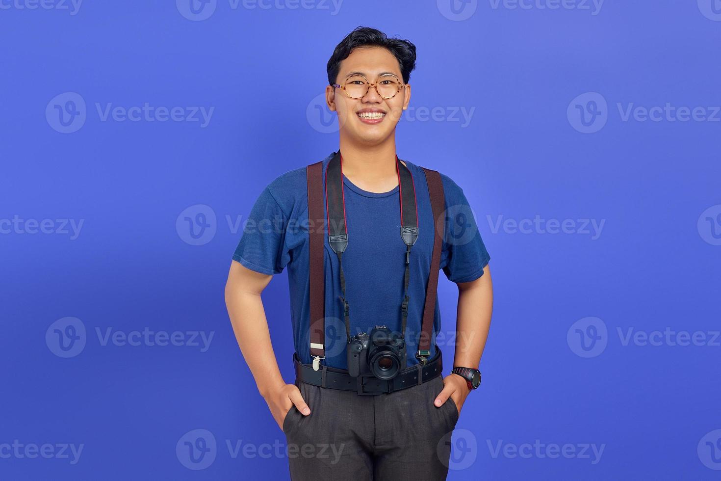 Fotógrafo guapo alegre y emocionado sosteniendo una cámara profesional sobre fondo púrpura foto