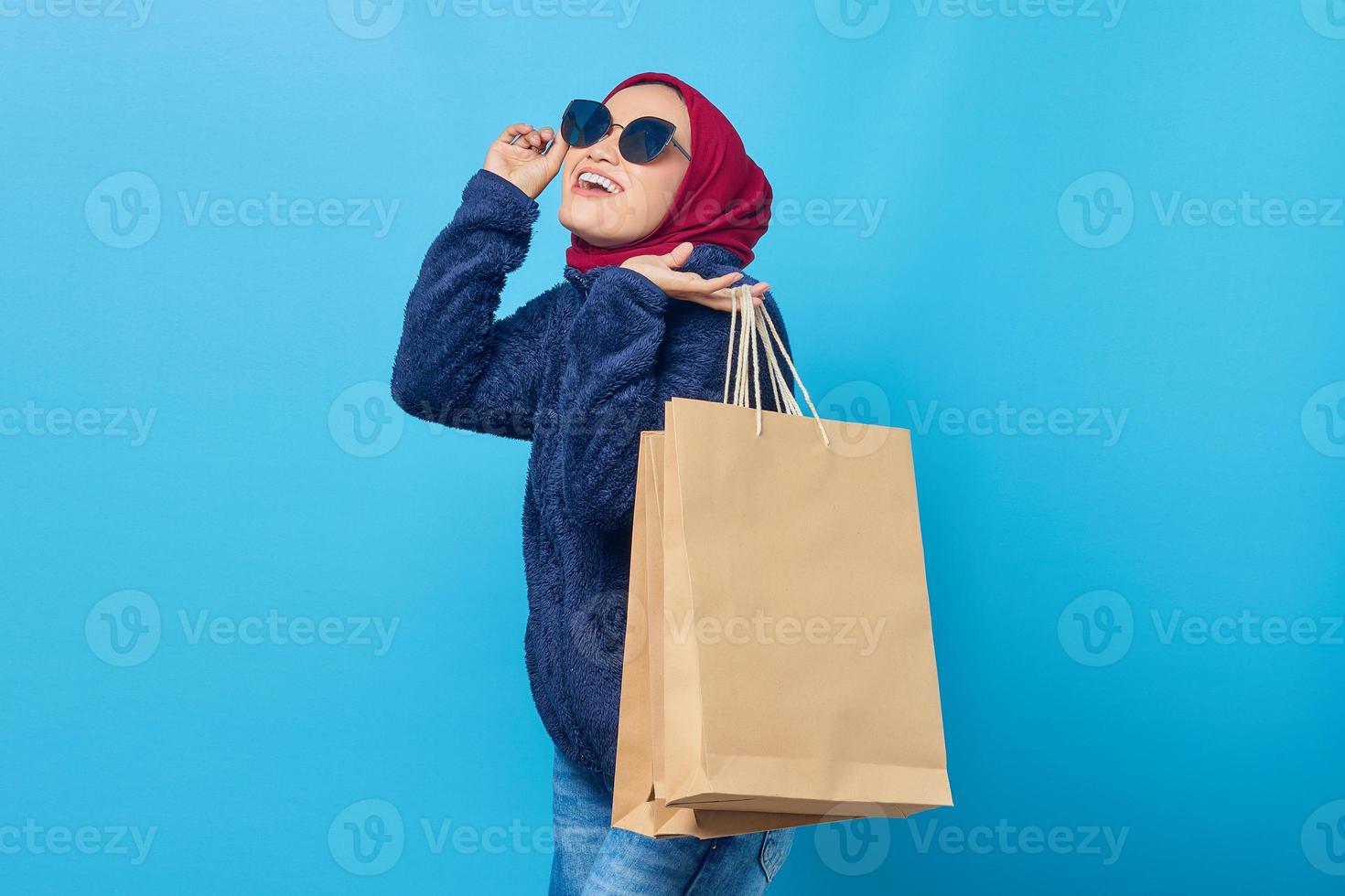 Alegre joven asiática con gafas de sol y sosteniendo bolsas de la compra sobre fondo azul. foto