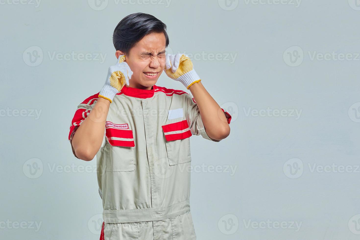 Retrato de frustrado joven apuesto mecánico cubriendo las orejas con los dedos sobre fondo gris foto