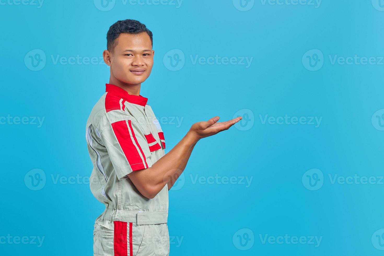 Portrait of smiling young Asian mechanic showing copy space in palm over blue background photo
