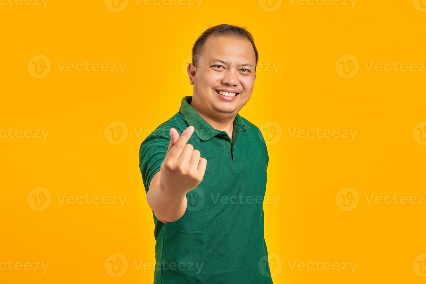 Portrait of smiling young Asian man showing finger heart over yellow background photo