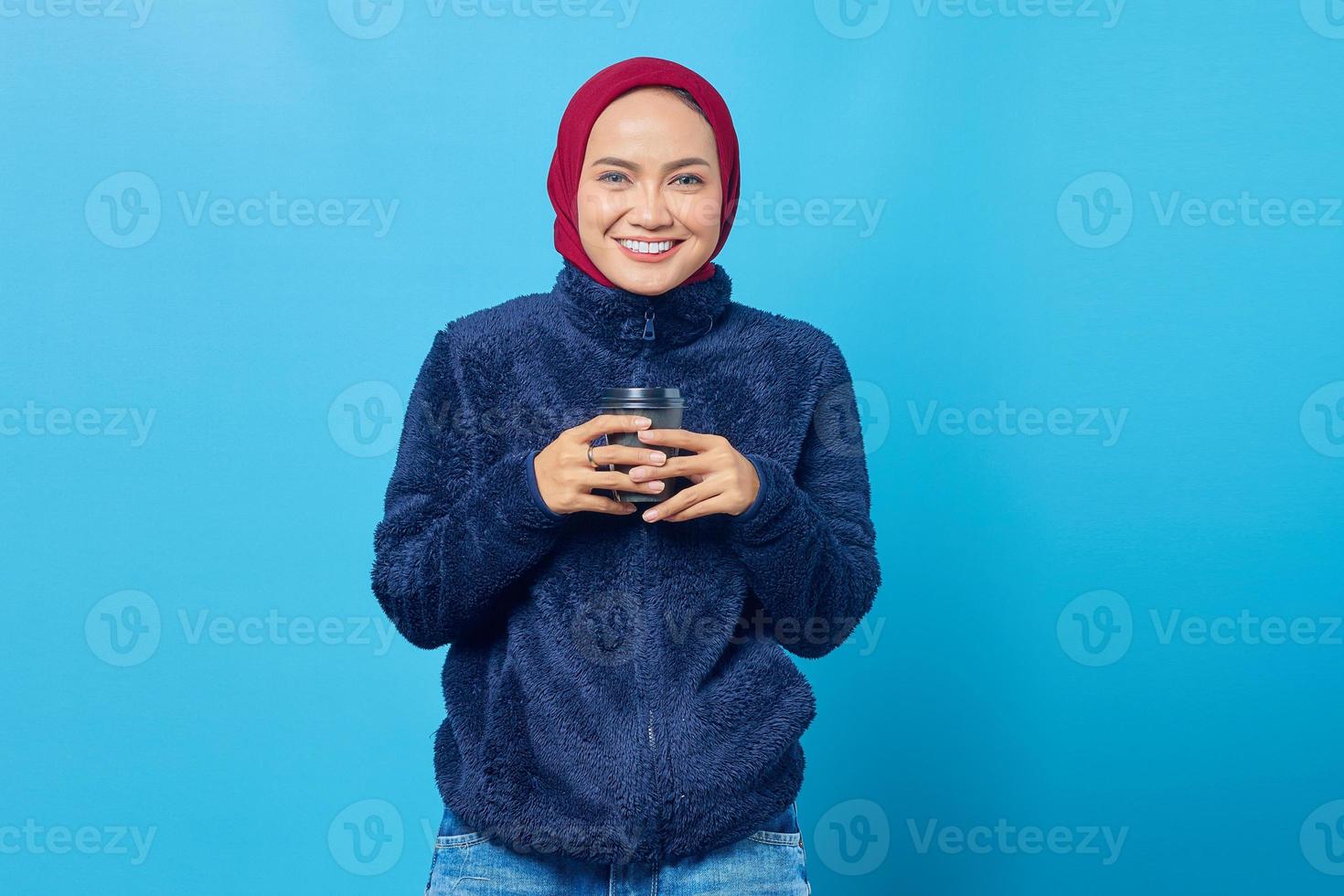 Alegre hermosa joven sosteniendo una taza de café sobre fondo azul. foto