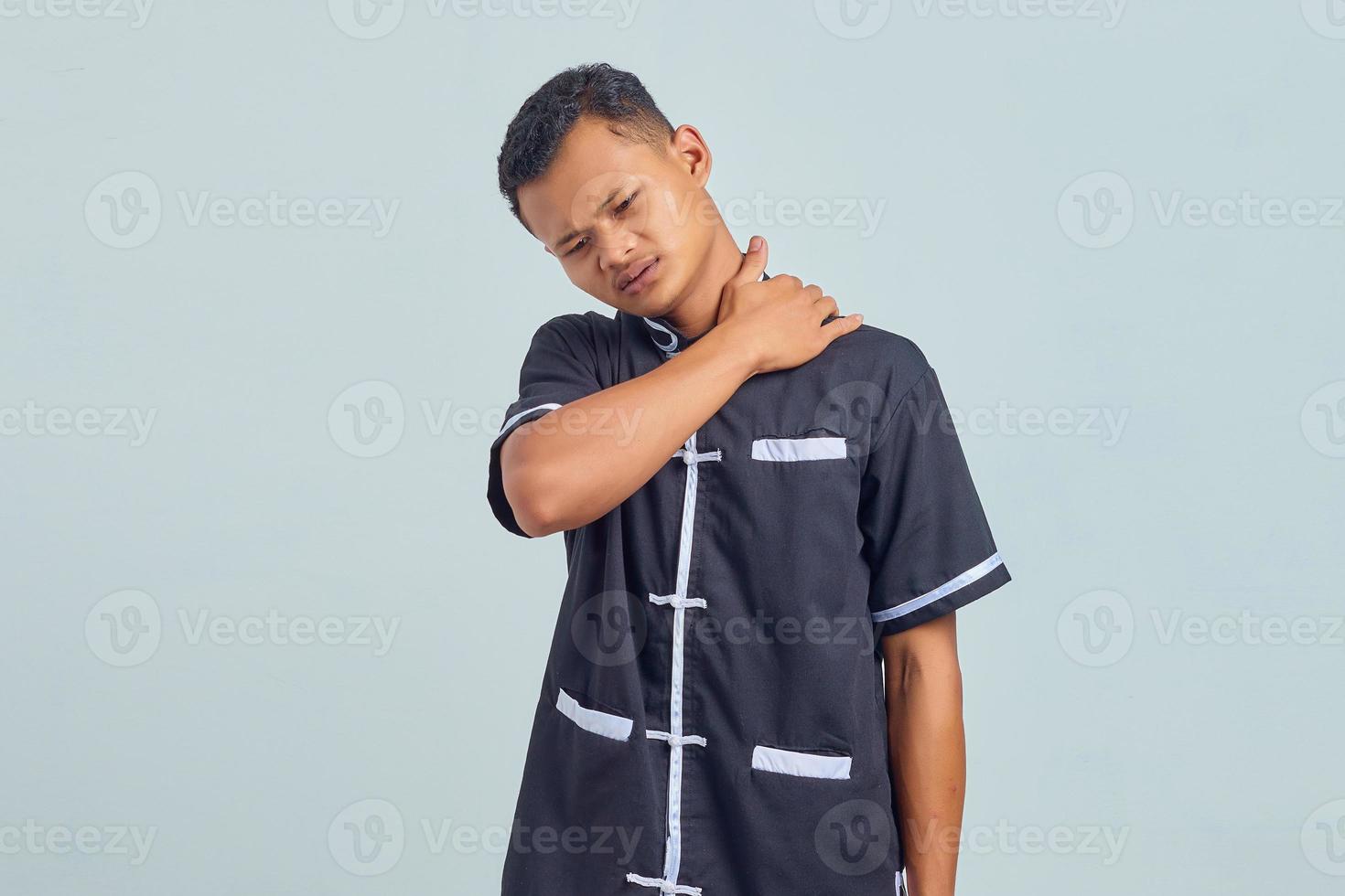 Retrato de joven asiático vistiendo uniforme de karate que sufren de dolor de cuello y tocar la espalda con las manos sobre fondo gris foto