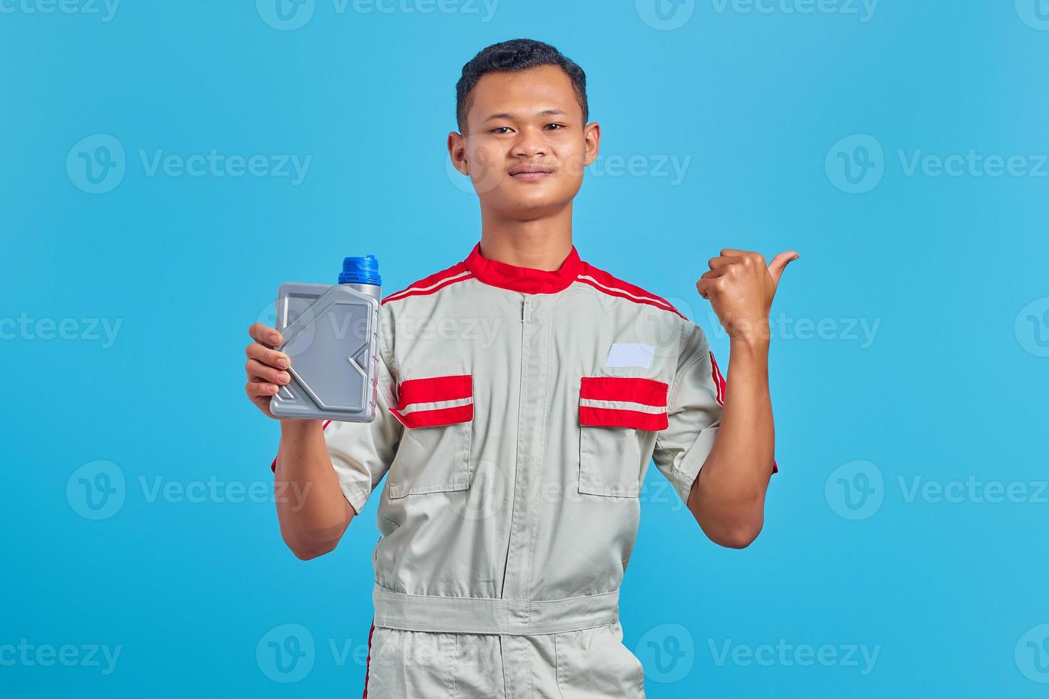 Portrait of smiling young Asian mechanic showing engine oil plastic bottle and pointing to empty space over blue background photo