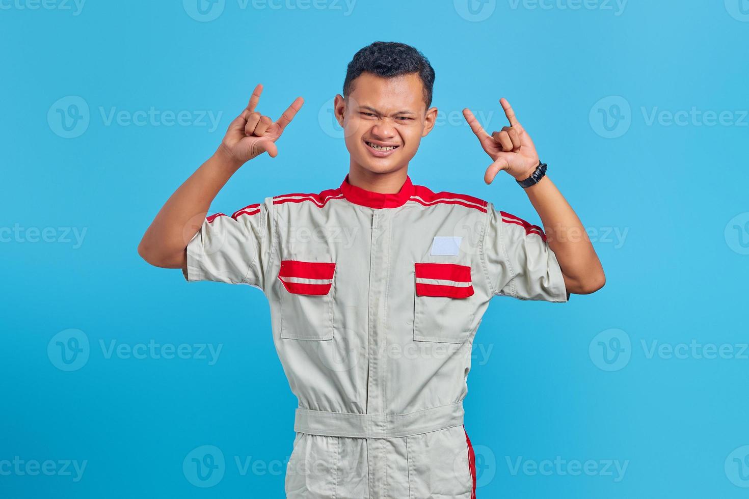 Portrait of young asian mechanic screaming with crazy expression doing rock symbol with hands over blue background photo