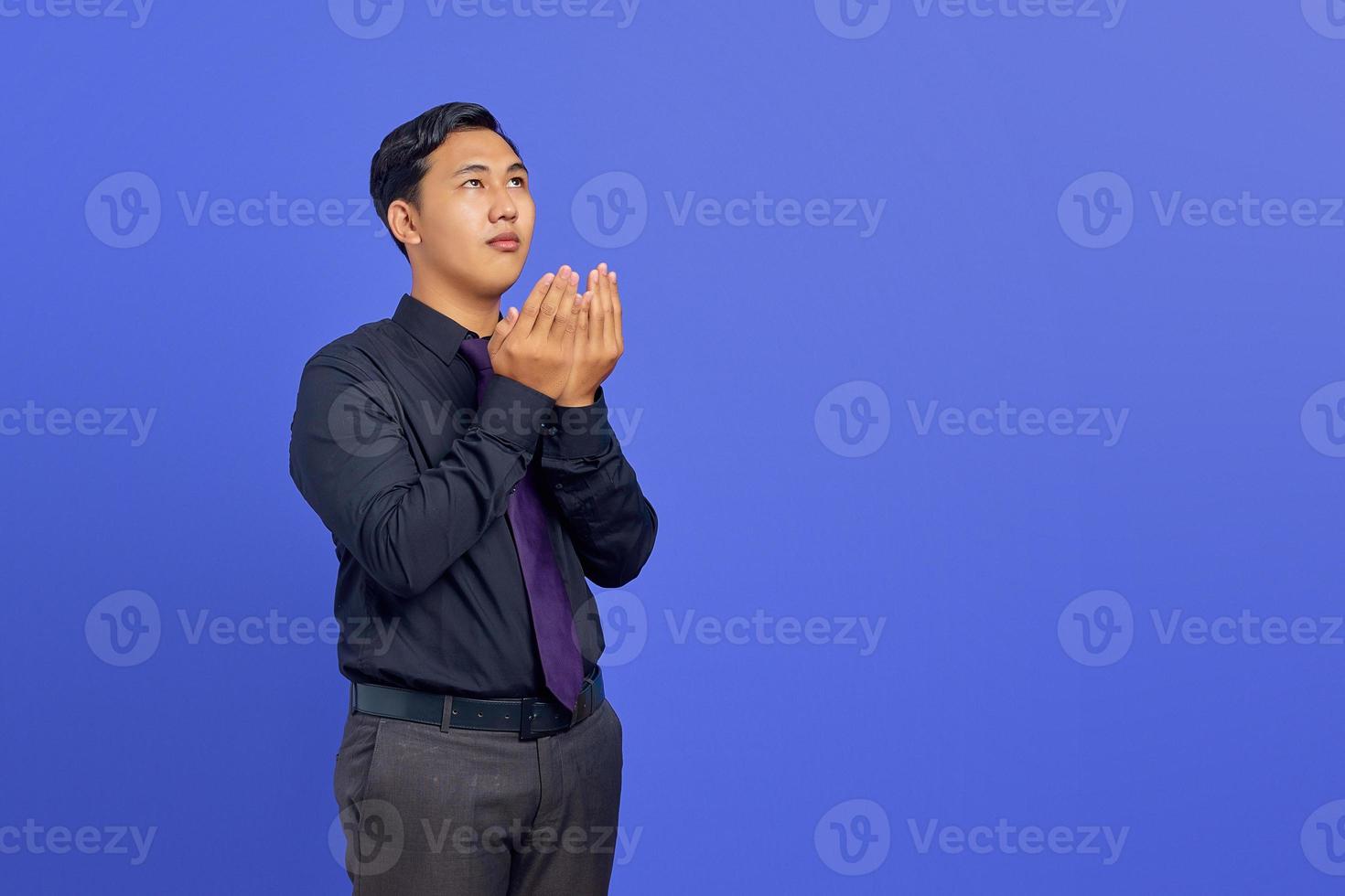 Photo of handsome businessman praying with expression wishing everything well on purple background
