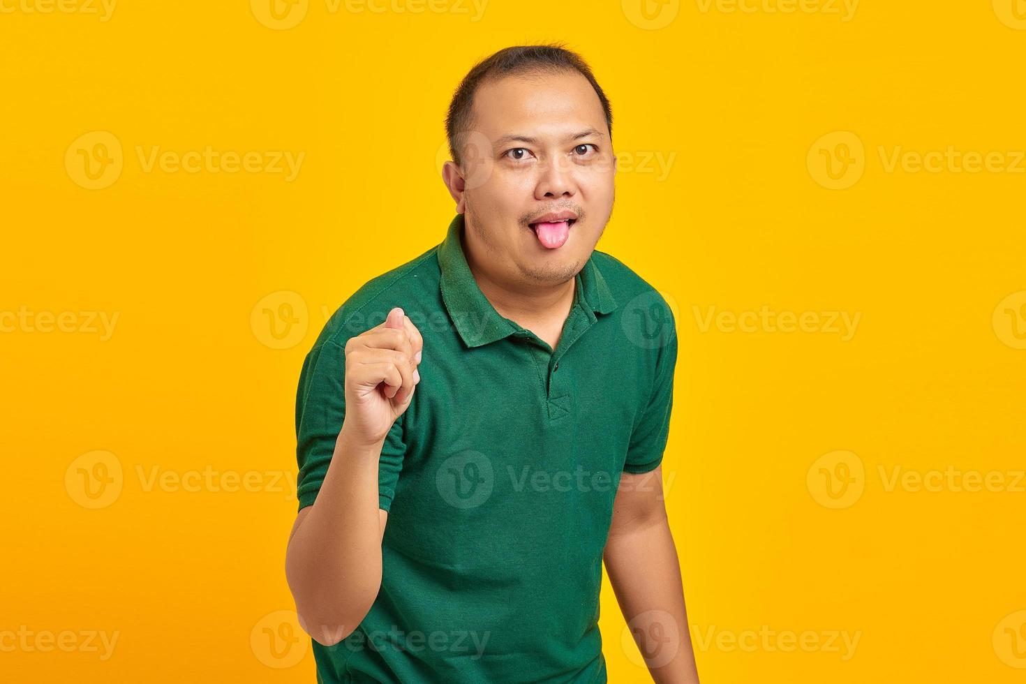 Portrait of asian man showing hand gesture folding fingers in front of camera with funny expression on yellow background photo