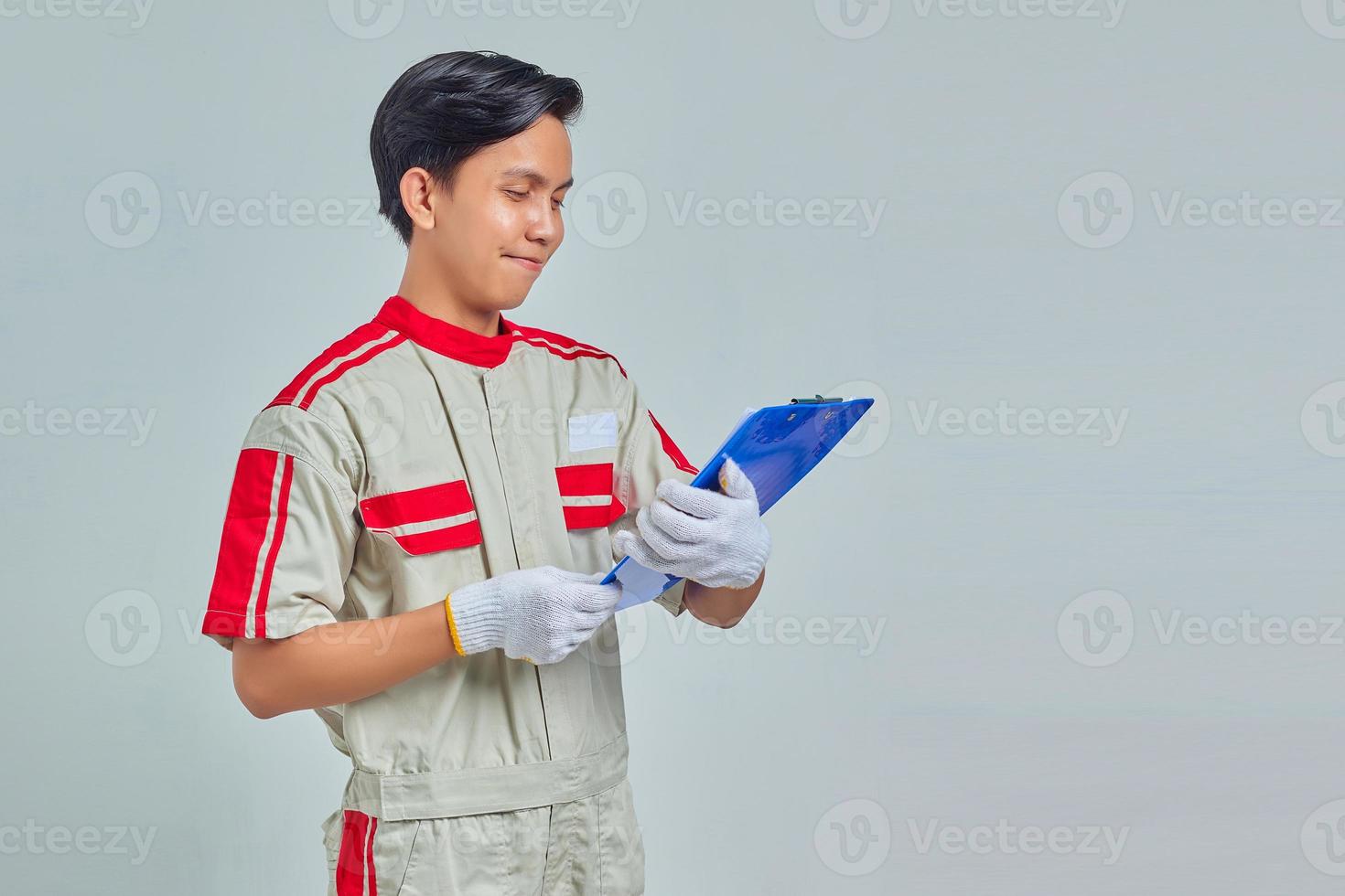 Feliz joven mecánico asiático sujetando el portapapeles aislado sobre fondo gris foto