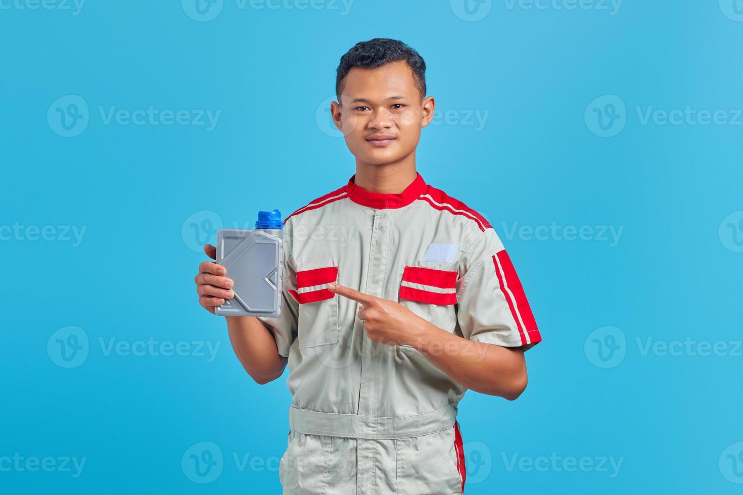 Portrait of smiling young Asian mechanic pointing at plastic bottle of engine oil with finger on blue background photo