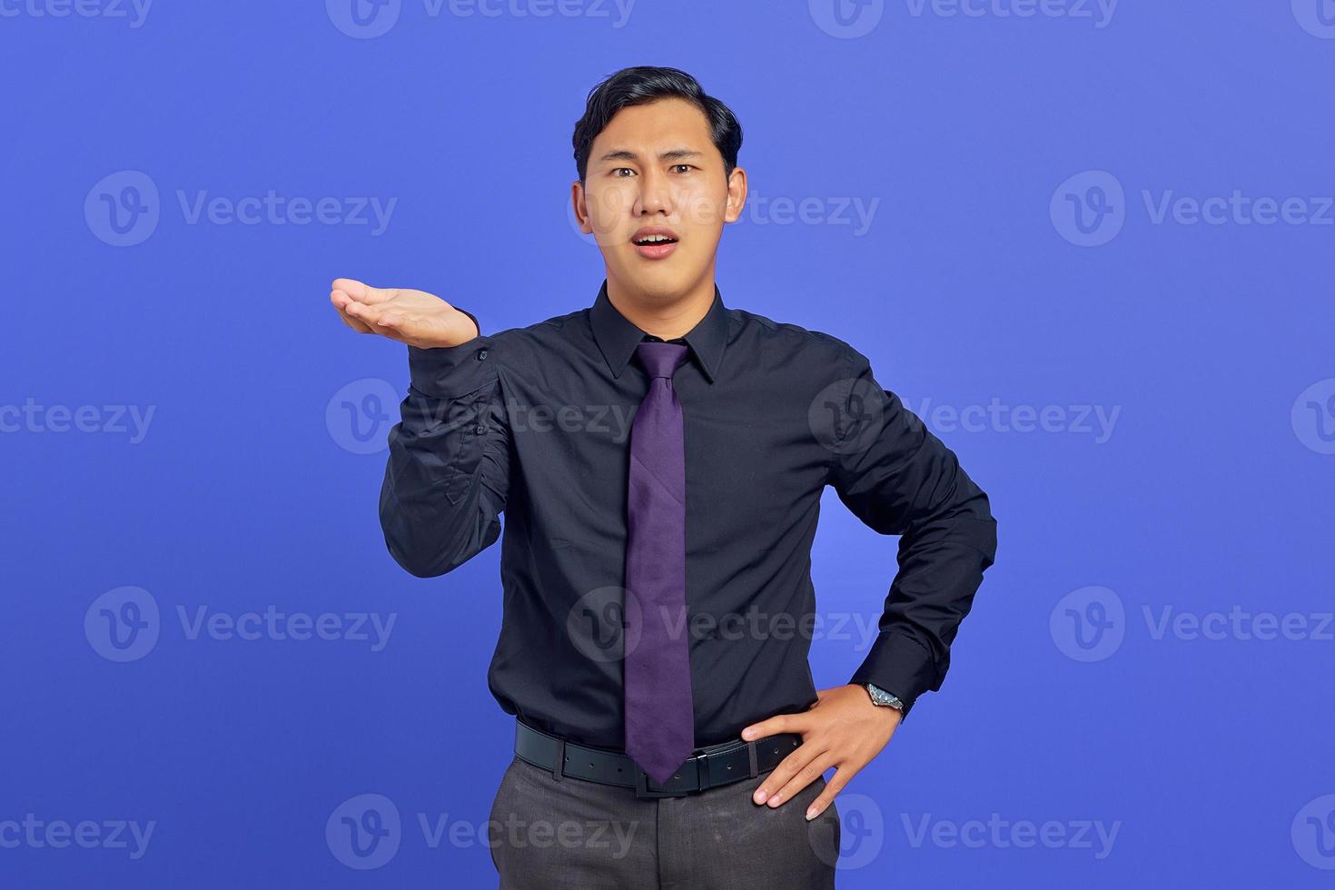 Portrait of shocked young handsome businessman showing copy space on palm on purple background photo