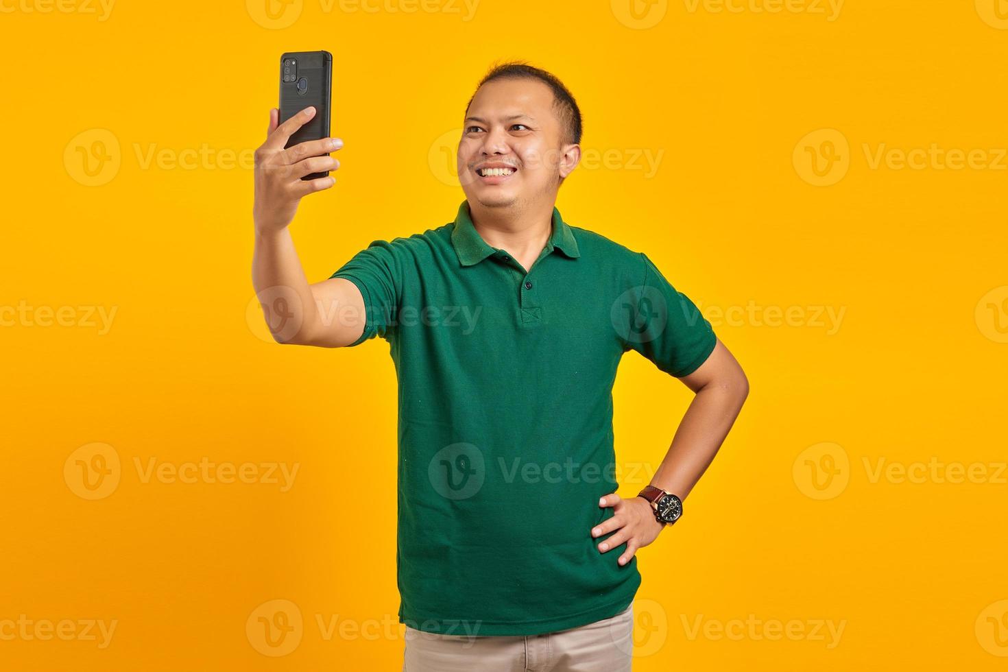 Cheerful young Asian man taking a selfie with a mobile phone on yellow background photo