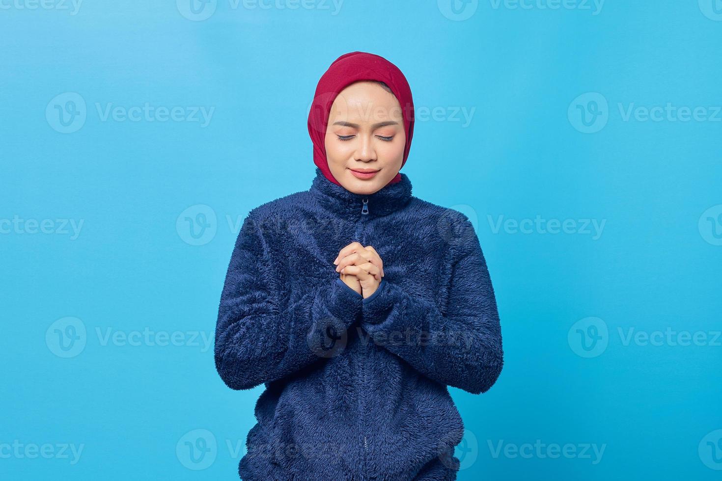 Atractiva joven asiática rezar y cerrar los ojos sobre fondo azul. foto
