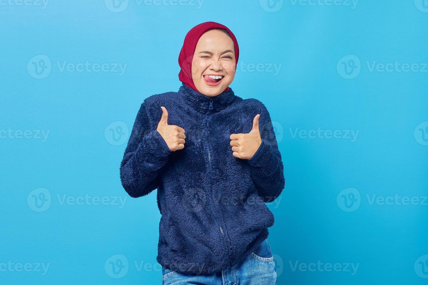 Portrait of excited cheerful young Asian woman showing thumbs up or approval sign on blue background photo