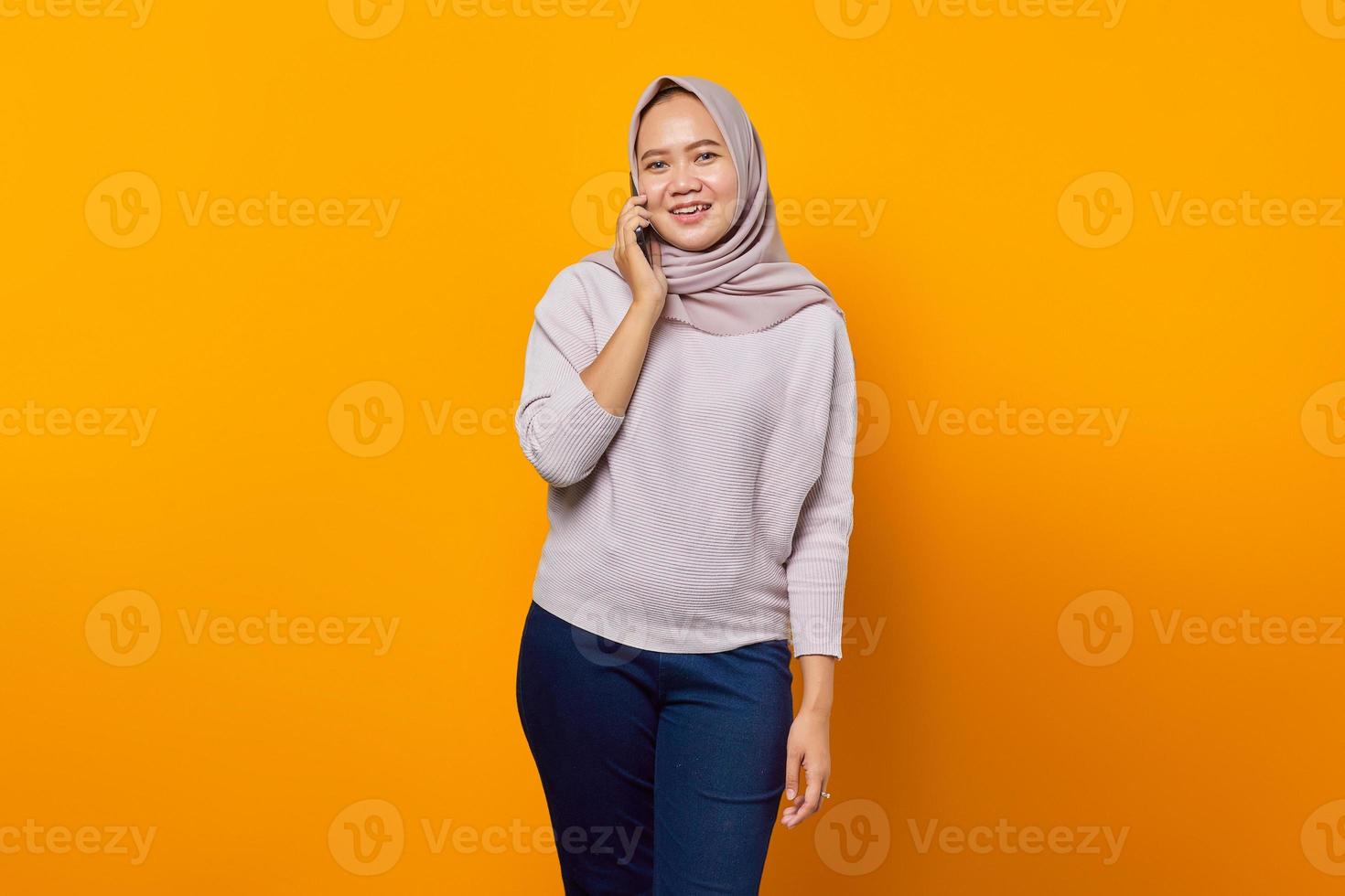 Portrait of cheerful young Asian woman talking on smartphone on yellow background photo