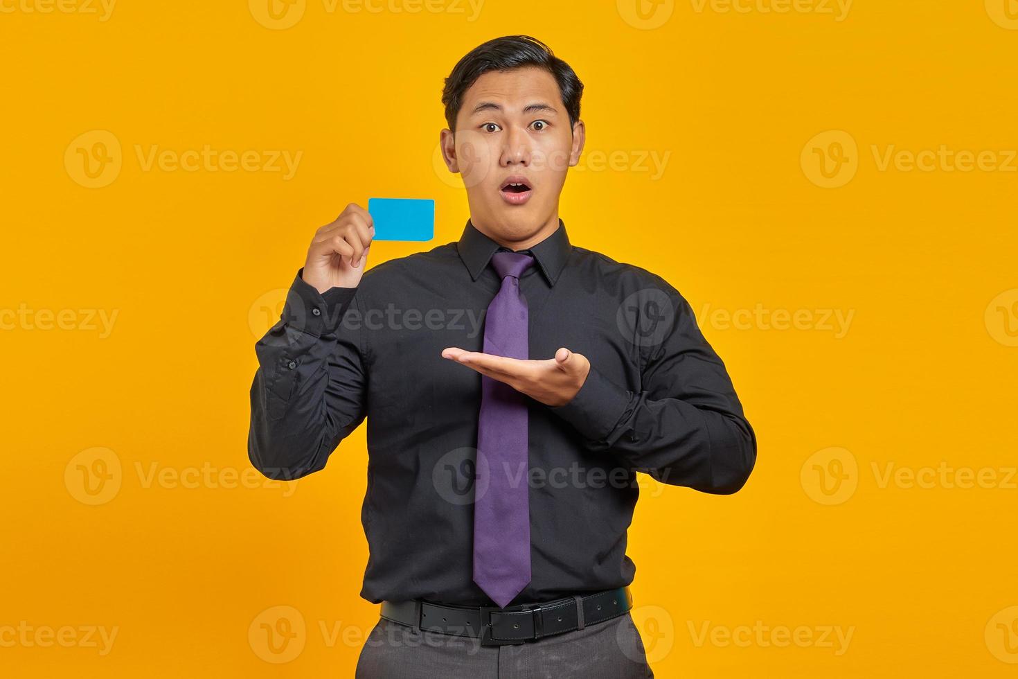 Surprised asian businessman showing credit card over yellow background photo