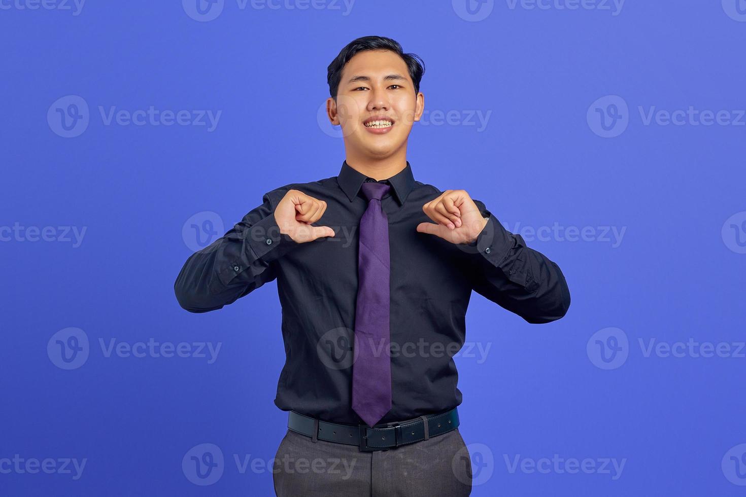 Sonriente joven asiático apuntando a sí misma con orgullo sobre fondo púrpura foto