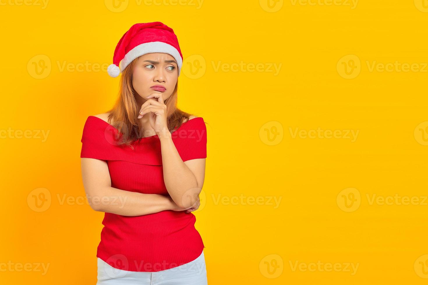 Pensive young woman wearing Christmas hat thinking about something and looking sideways photo