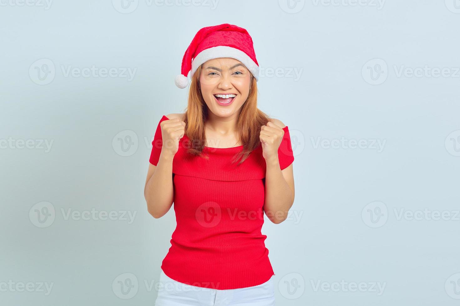 Emocionada joven asiática celebrando el éxito con las manos levantadas sobre fondo blanco. foto