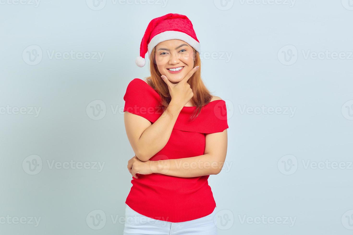 Smiling young Asian woman crossed one arm and put another hand on a chin on white background photo