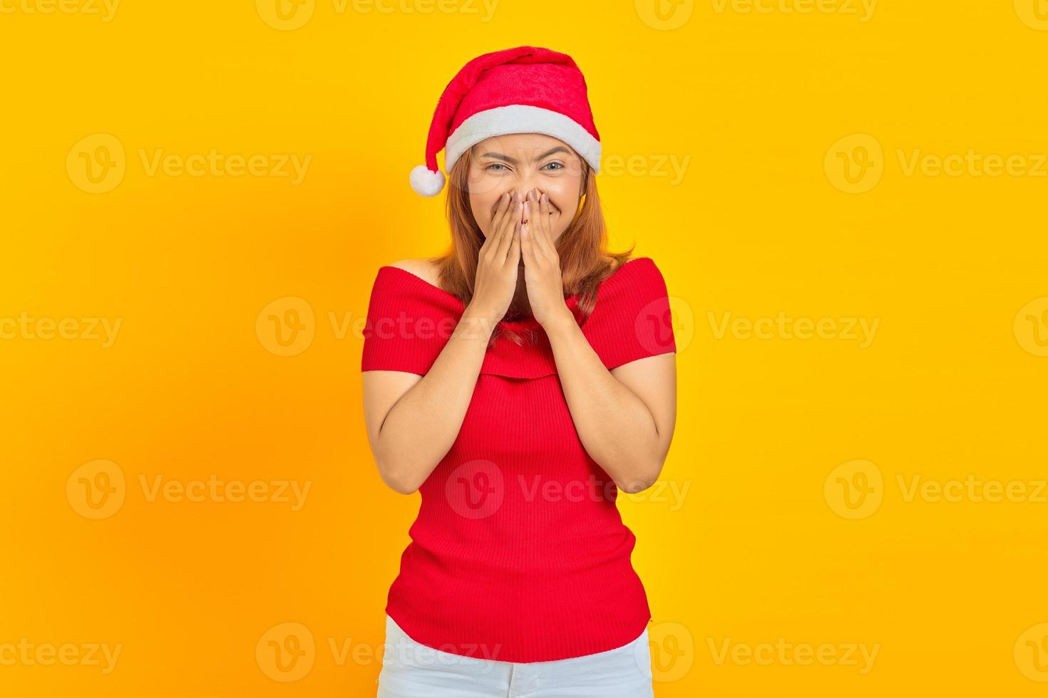 Retrato de risa joven mujer asiática vistiendo gorro de navidad cubriendo la boca con la mano foto