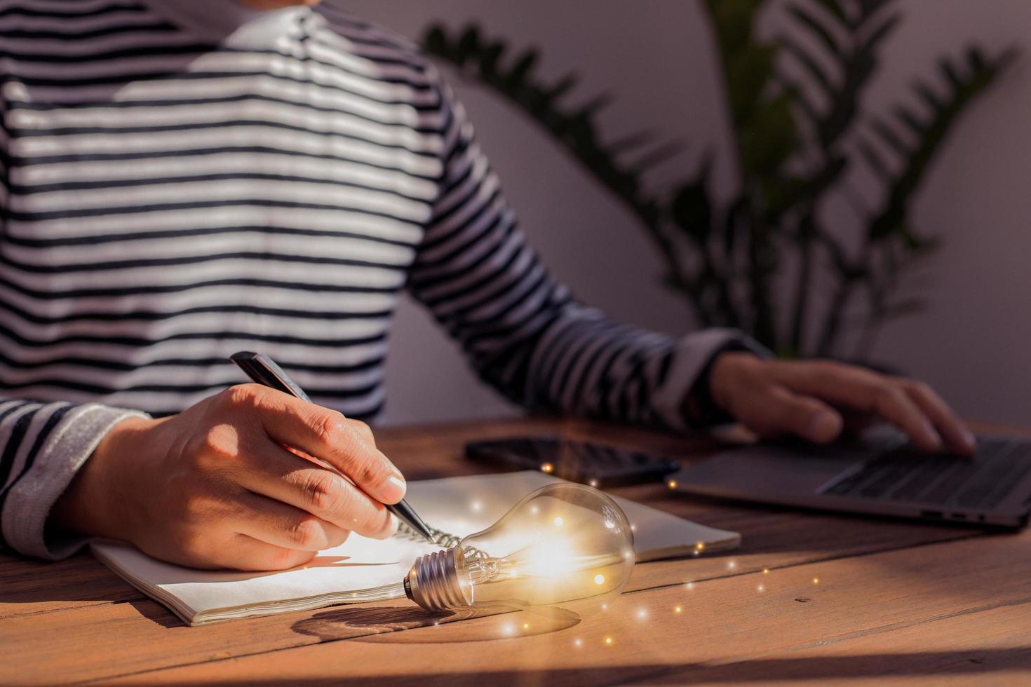 Man's hand writing on table book with light bulb, online technology-inspired concept. concept, idea, innovation photo