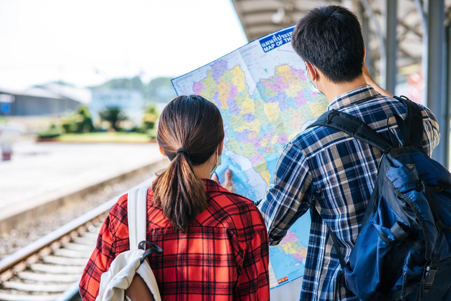 Male and female tourists look at the map beside the railway tracks. photo