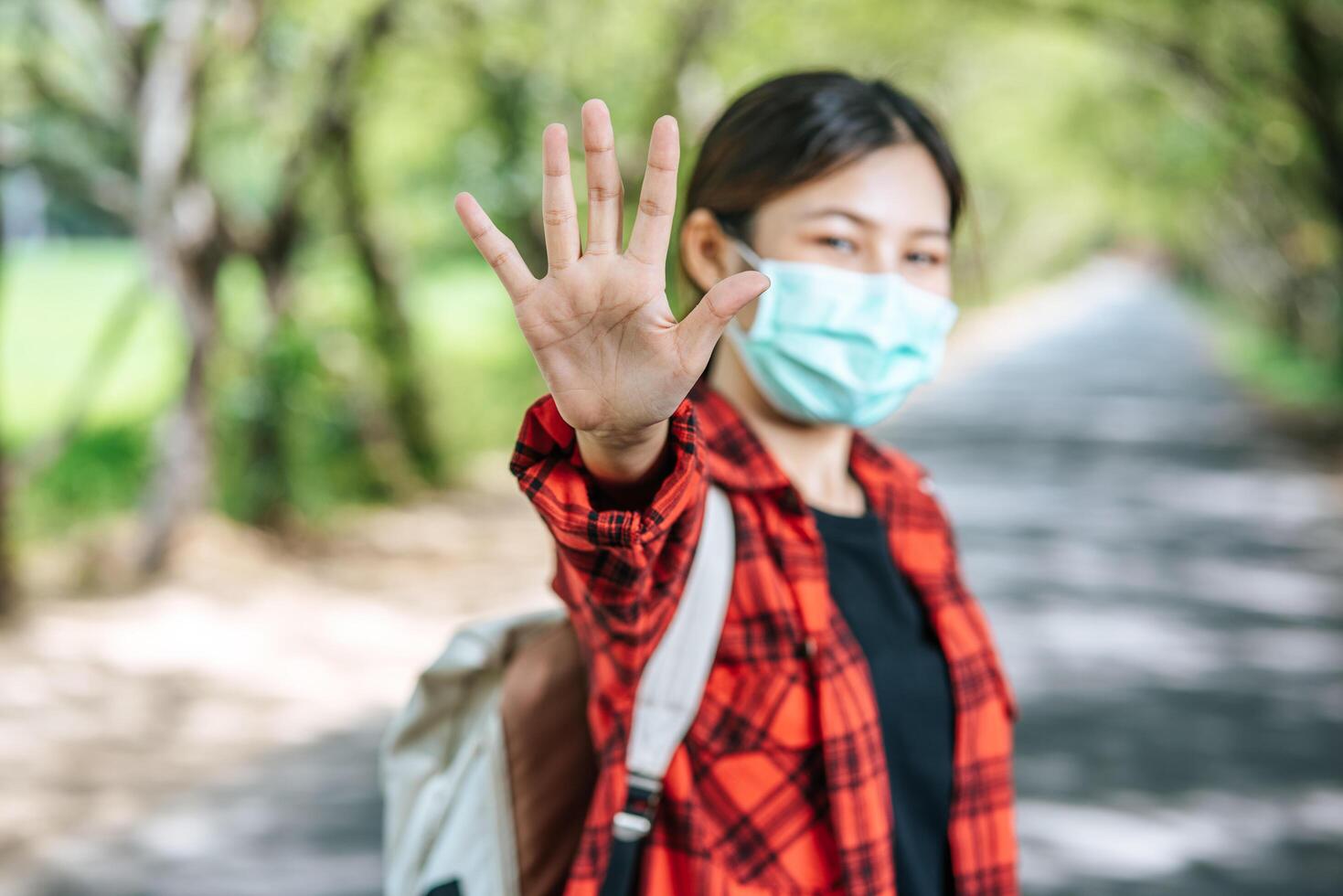 A female tourist carrying a backpack and raising her five fingers to ban on the road. photo