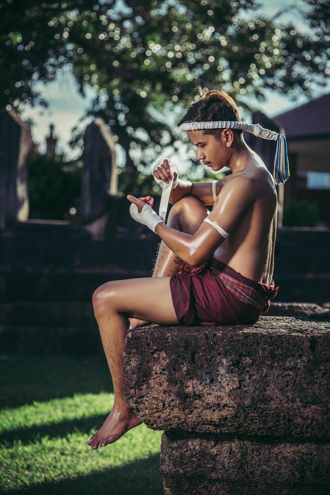 The boxer sat on the stone, tied the tape around his hand, preparing to fight. photo