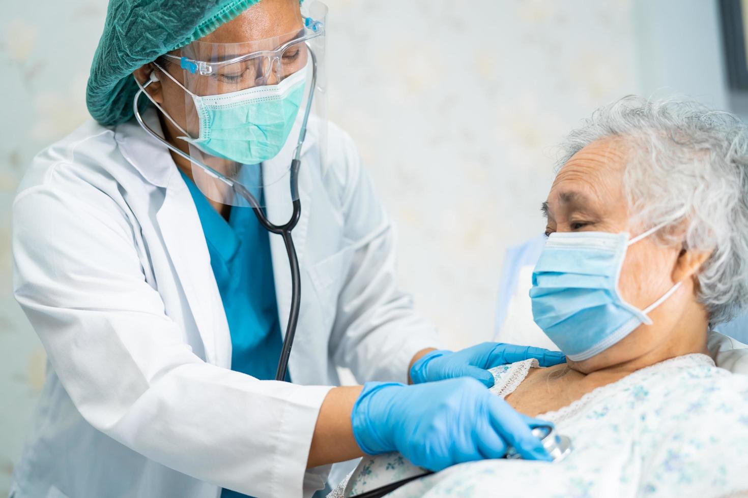 Asian doctor wearing face shield and PPE suit new normal to check patient protect safety infection Covid-19 Coronavirus outbreak at quarantine nursing hospital ward. photo