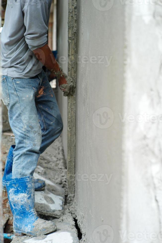 Selective focus on the surface of cement wall with blurred hands of worker plastering the cement in background photo