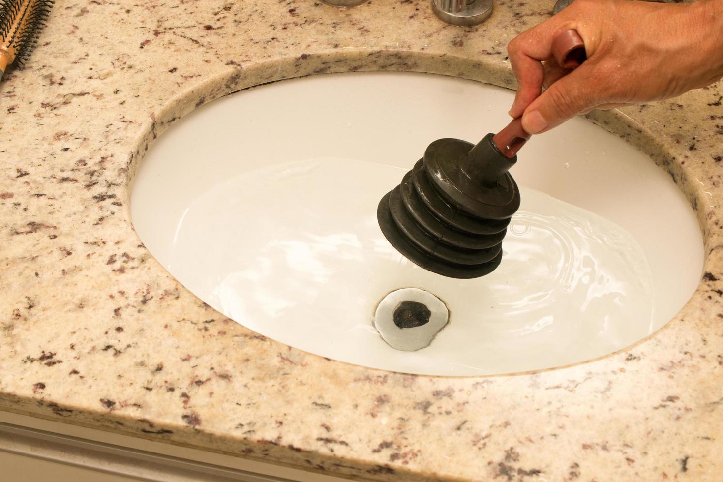 Hombre usando un desatascador para destapar el lavabo del baño foto