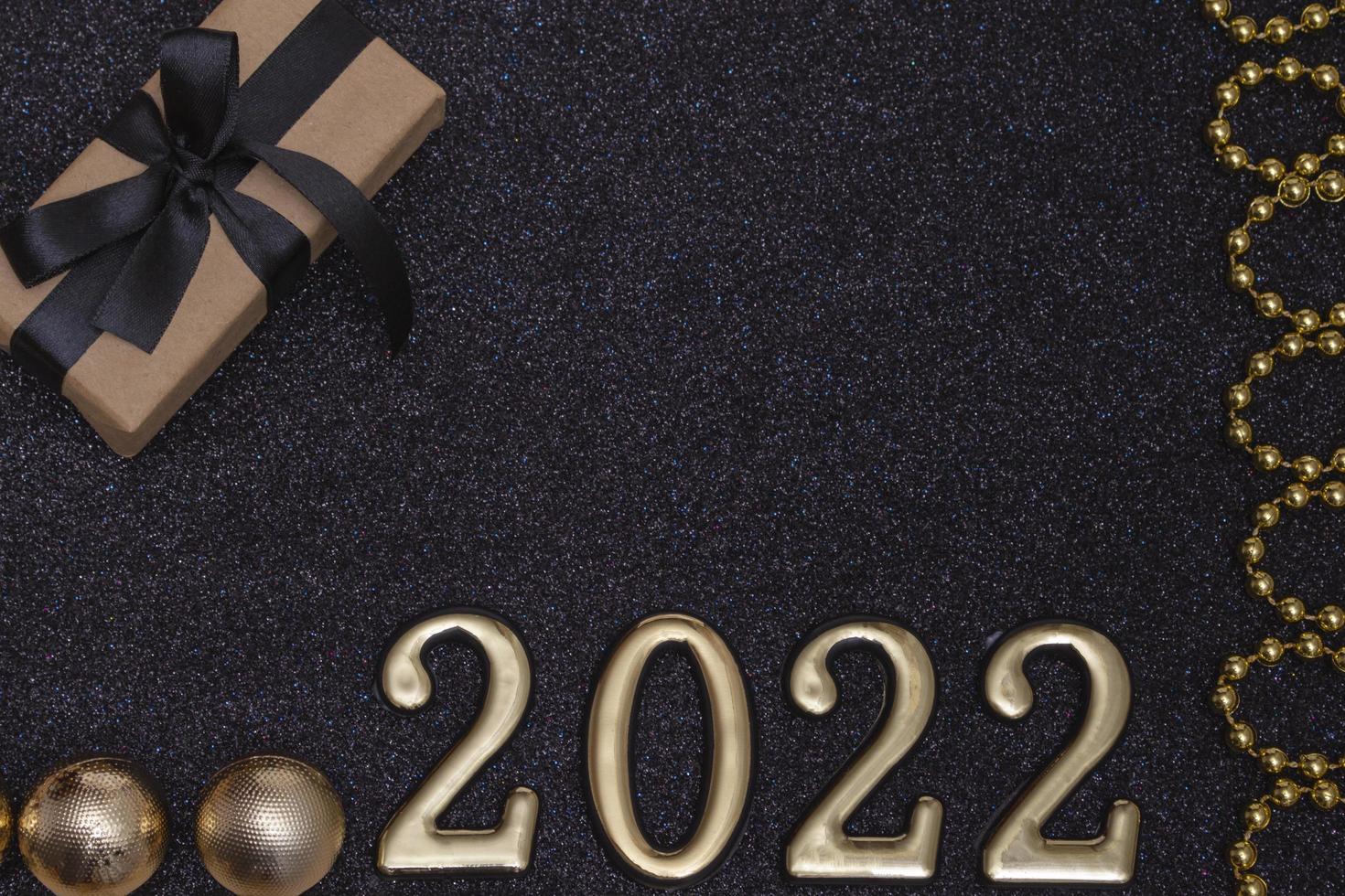 New Year 2022. Top view New Year mockup on black shiny background red ribbon, gift box, gold numbers and multicolored sparkles. Layout of postcards photo