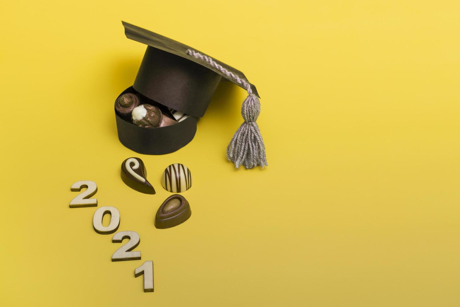A box of chocolates in the form of a graduate hat. Chocolate day concept. Graduation 2021 on colored background. photo