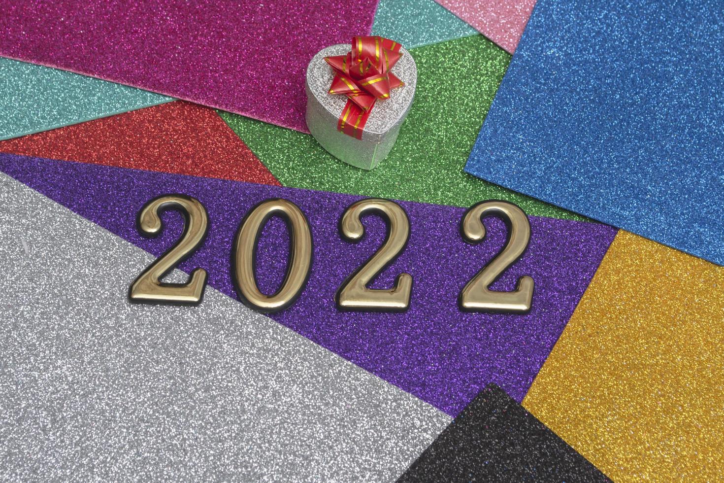 sobre un fondo de año nuevo brillante colorido brillante, una caja de regalo plateada con un lazo rojo y números dorados 2022. concepto para la tarjeta de año nuevo. foto