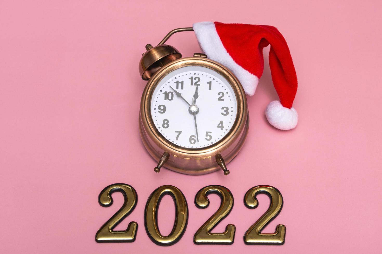 New year concept on pink background alarm clock in santa hat with golden numbers 2022 photo