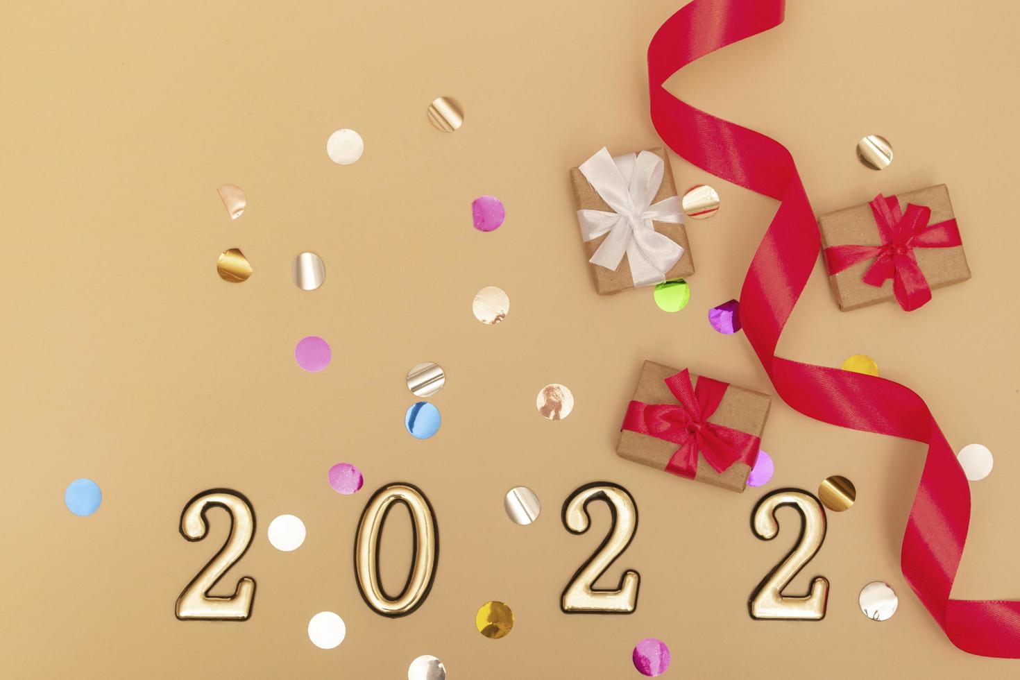 New Year 2022. Top view New Year mockup on beige background red ribbon, gift box, gold numbers and multicolored sparkles. Layout of postcards, invitations. photo