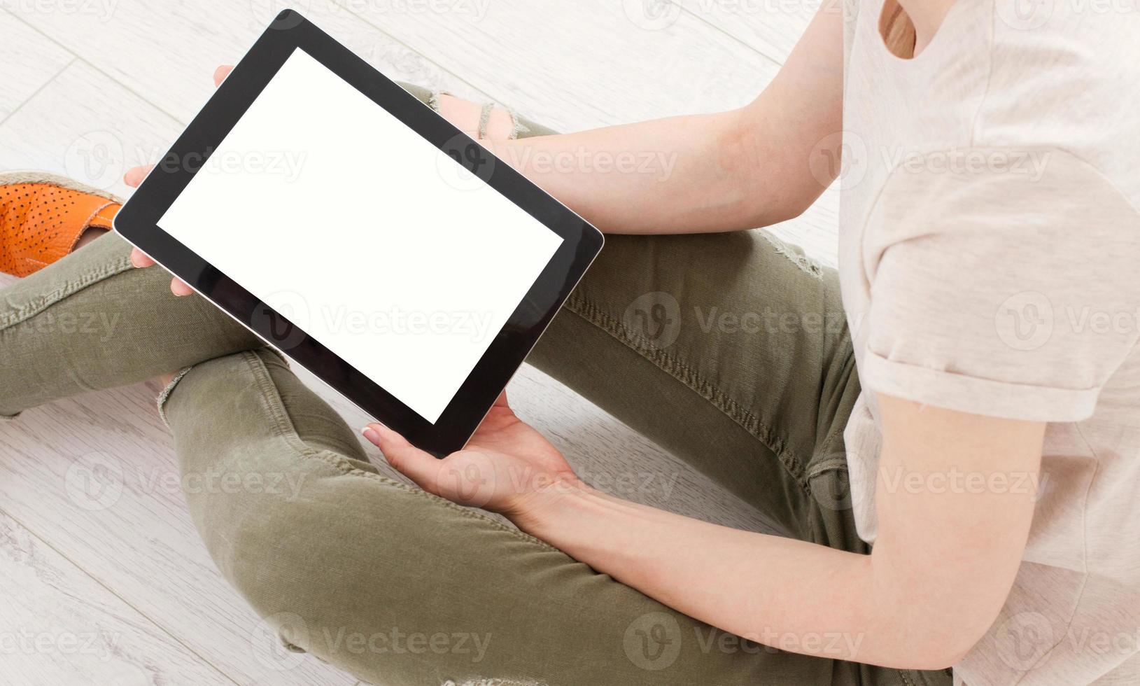Chica adolescente con un tablet pc sentado en el suelo de una sala de estar, tocando la pantalla en blanco foto