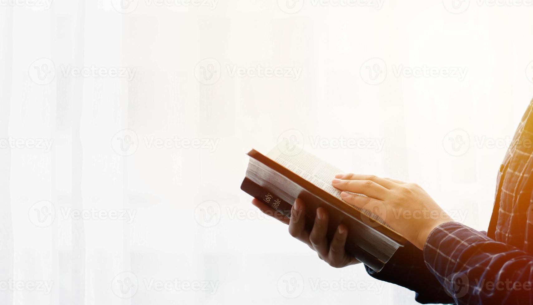 Leer el primer plano de la Biblia de la mano de una mujer leyendo la Biblia junto a la ventana fondo blanco. foto