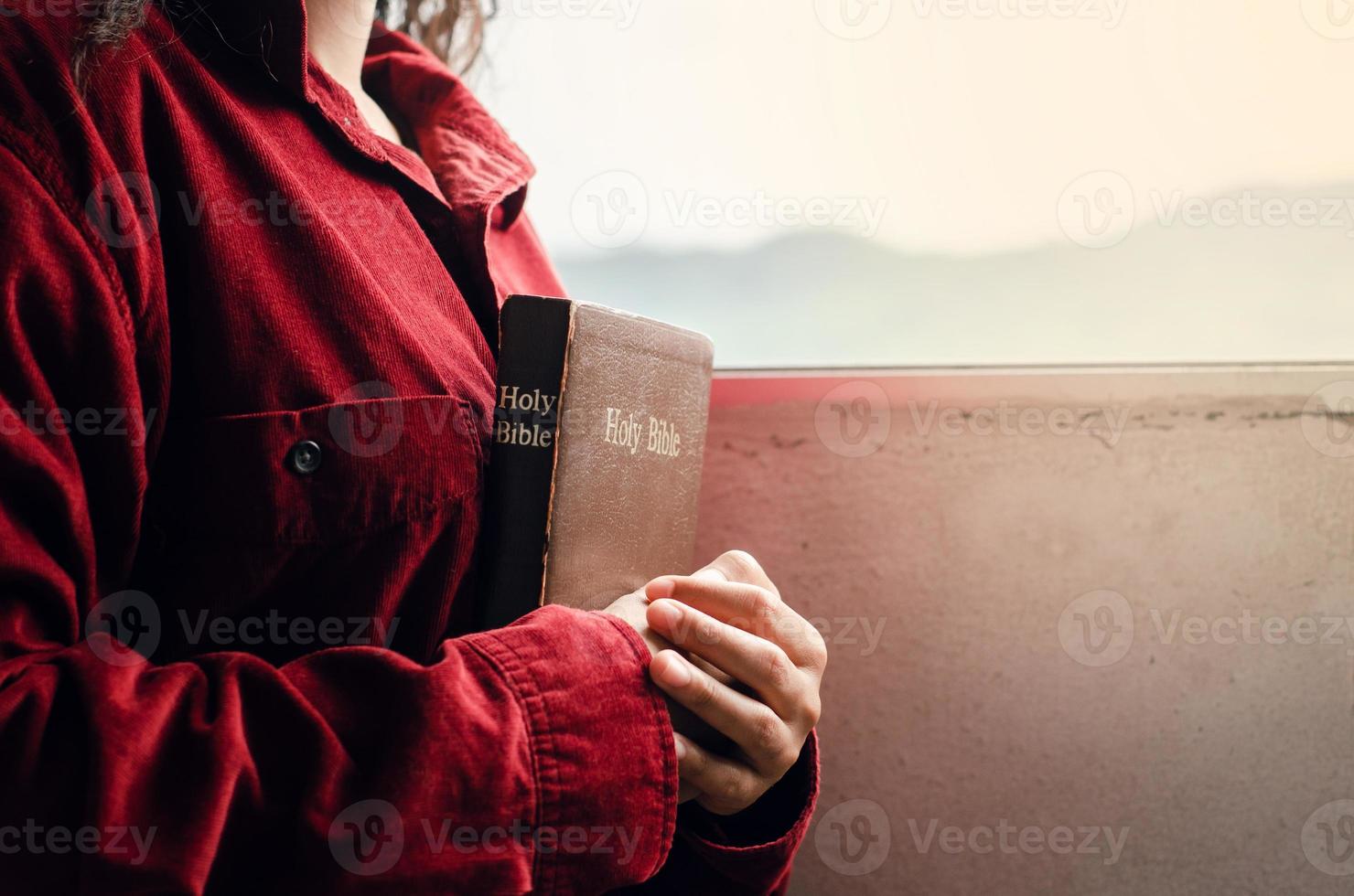 una adolescente vestida con una blusa roja está orando por la bendición de dios. tenga una vida mejor una mujer abraza la biblia con una biblia junto a la ventana, hermosa vista, una crisis en la vida cristiana foto