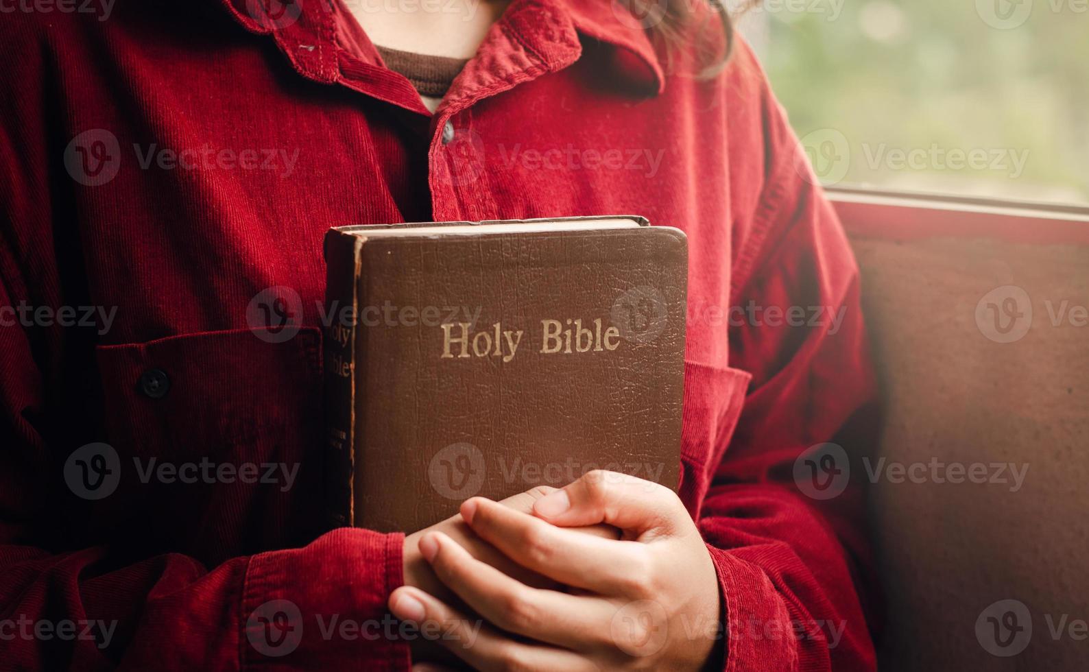 A teenage girl wearing a red blouse is praying for the blessing of God. Have a better life A woman embraces the Bible With a Bible by the window, beautiful view, a crisis in the Christian life photo