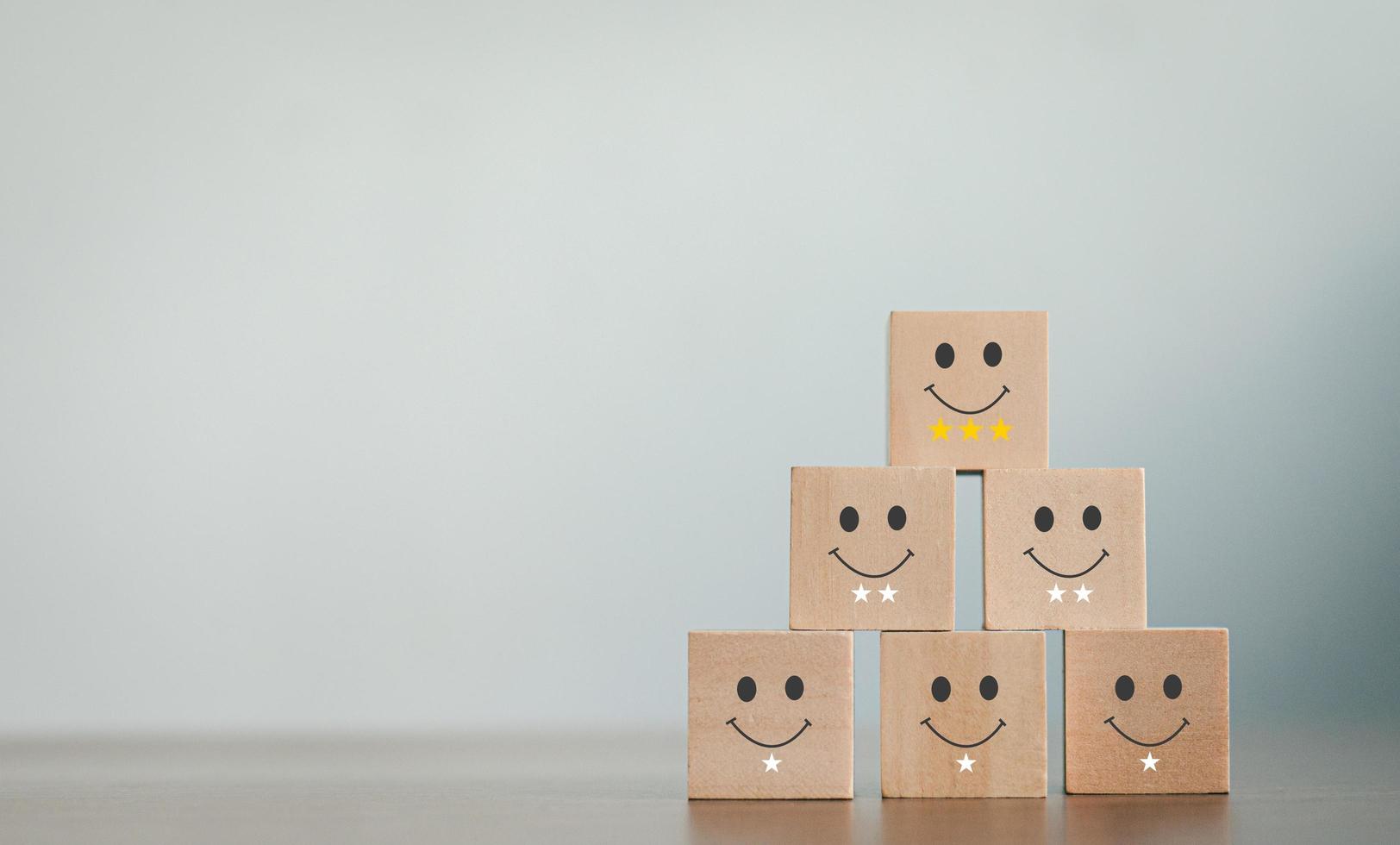 A wooden blog on customer service assessment concepts and satisfaction surveys. The customer selects a smiley face icon and a star symbol lined up on the upper wooden block of the wooden cube photo