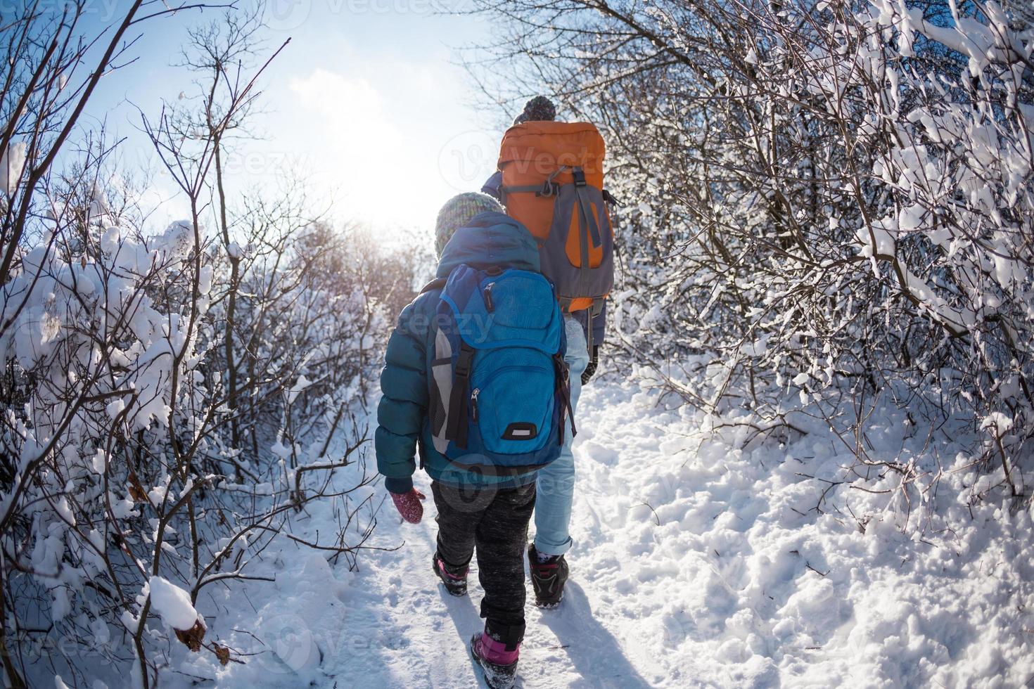 A child with a backpack walks with mother in a snowy forest photo