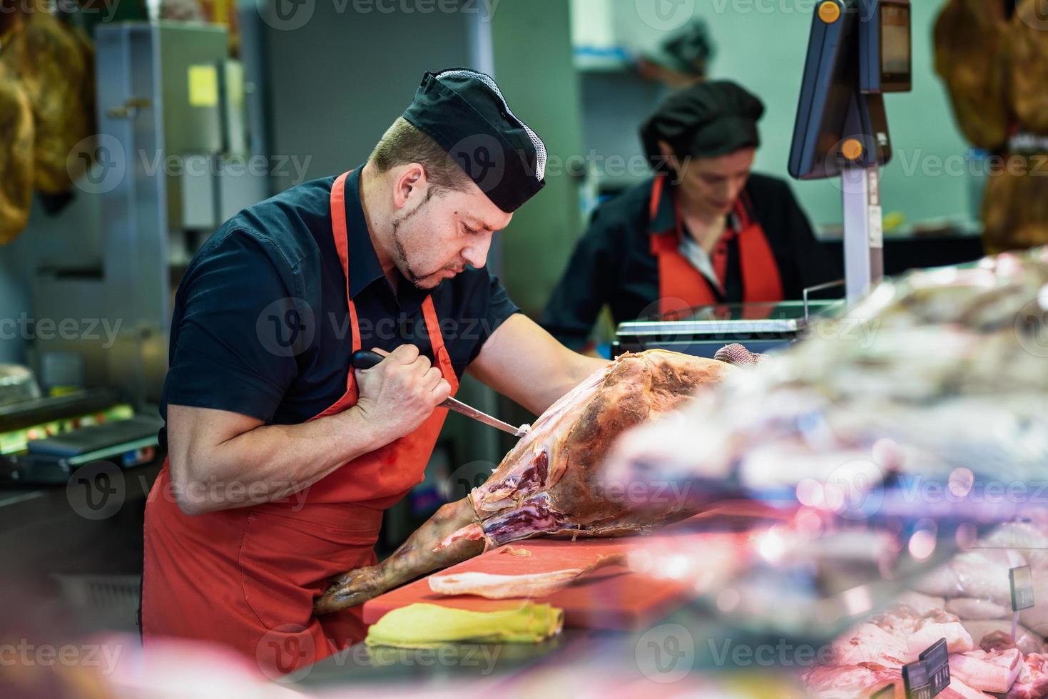 Carniceros deshuesando un jamón en una carnicería moderna foto