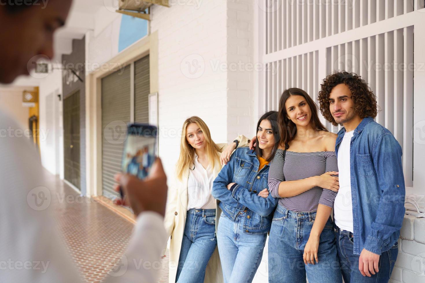 Multi-ethnic group of friends taking photos with a smartphone in the street.