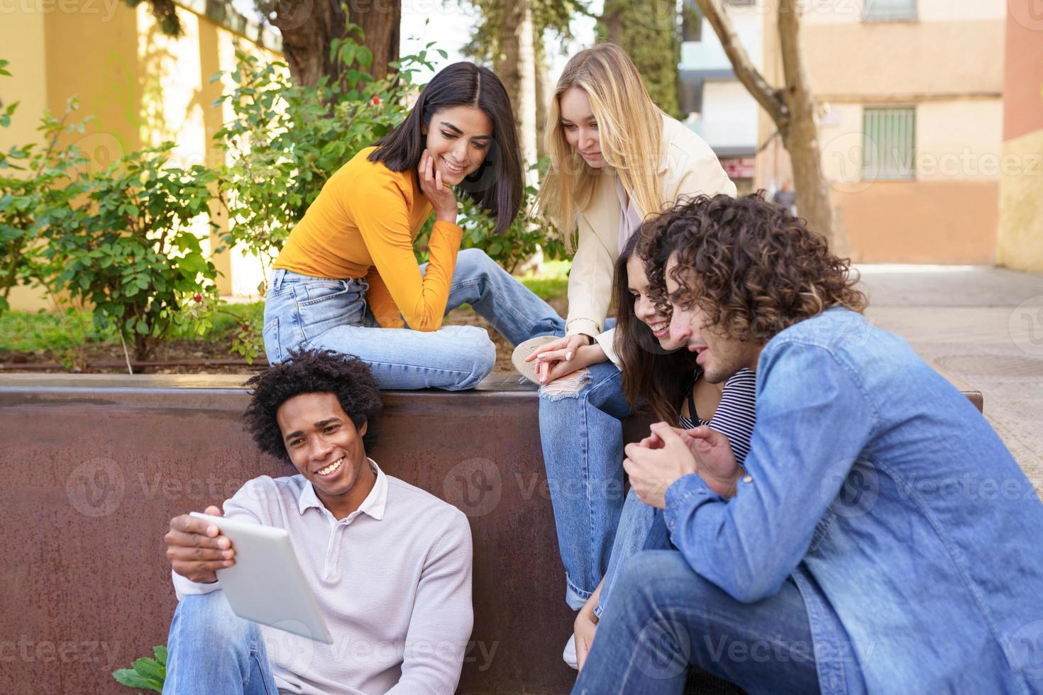 grupo multiétnico de jóvenes mirando una tableta digital al aire libre en el contexto urbano. foto