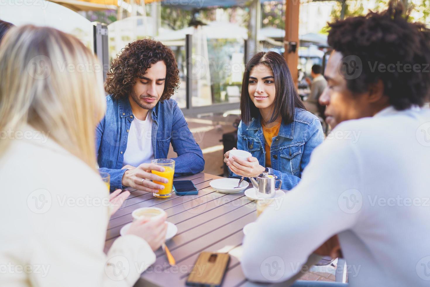 Grupo multiétnico de estudiantes tomando una copa en la terraza de un bar de la calle. foto