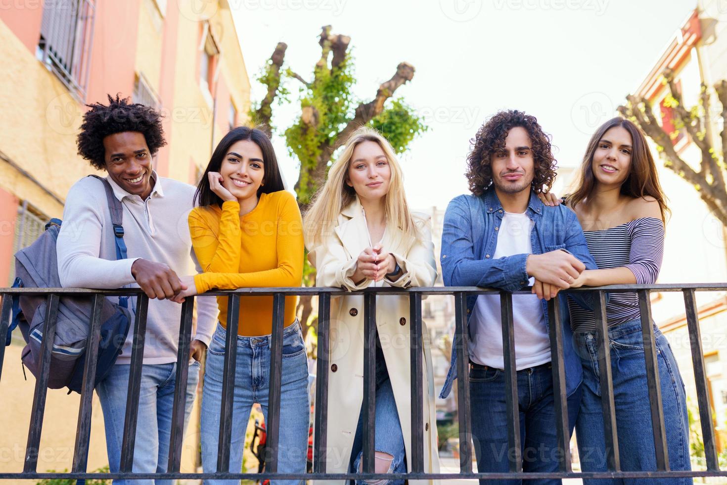 Grupo multiétnico de amigos reunidos en la calle apoyados en una barandilla. foto